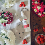 Black Raspberry & Peppercorn scented luxury frosted glass room spray surrounded by fresh flowers, peppercorns and raspberries sitting on a cosy blanket