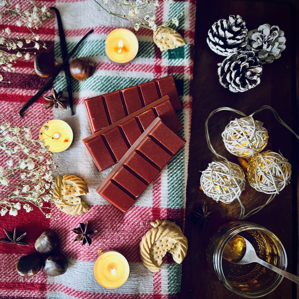 Red coloured Christmas Cookie scented snapbar wax melts on a checkered cloth surrounded by festive biscuits, chestnuts, caramel and pine cones.