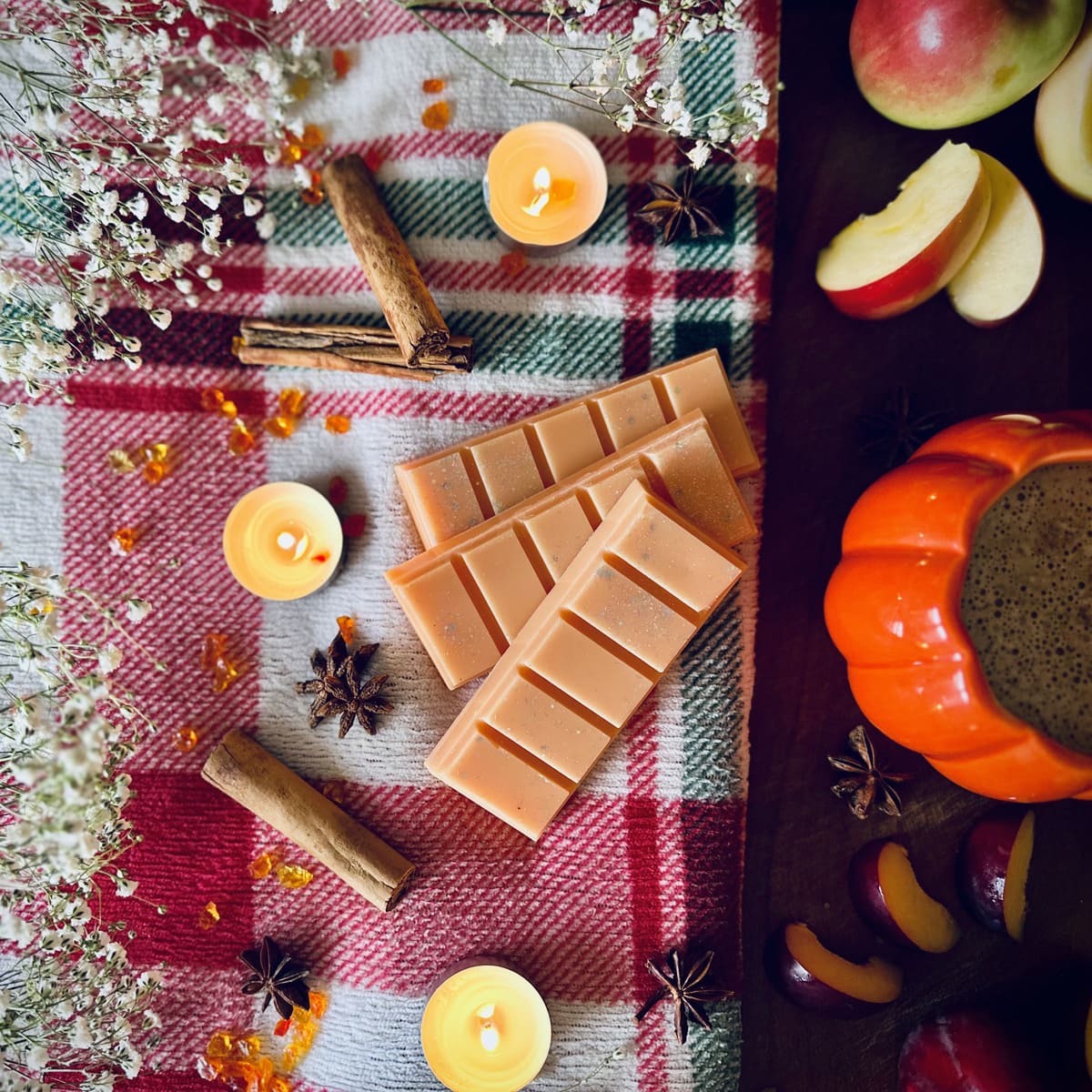 Orange coloured Frosted Pumpkin scented snapbar wax melts on a red festive plaid tablecloth with candles, apples, and pumpkins.