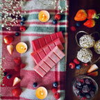 Red coloured Frosty Berries scented snapbar wax melts on a checkered cloth surrounded by winter berries, Christmas lighs and tea lights