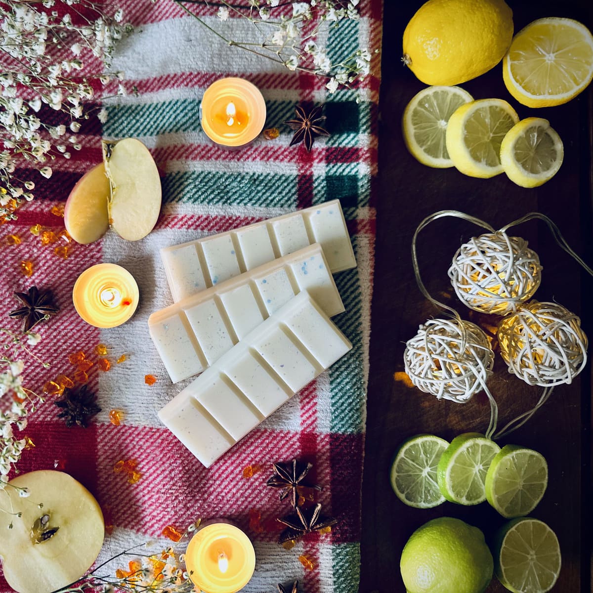 White coloured Frosty Lake scented snapbar wax melts on a red festive plaid cloth with candles, apples, and lemons.