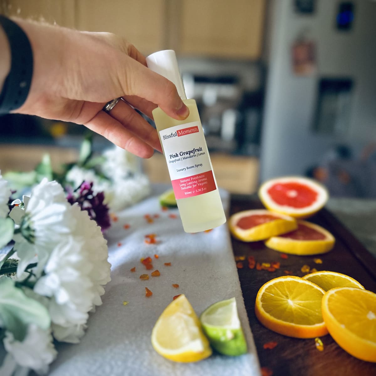 Hand holding a luxury Pink Grapefruit frosted glass room spray surrounded by citrus fruits and flowers