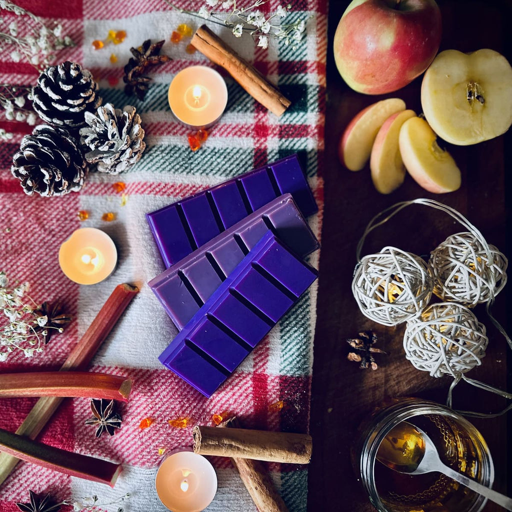Purple coloured Rhubarb and cinnamon scented snapbar wax melts with candles, apples, and decorative elements on a festive checkered cloth.