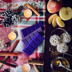 Purple coloured Rhubarb and cinnamon scented snapbar wax melts with candles, apples, and decorative elements on a festive checkered cloth.