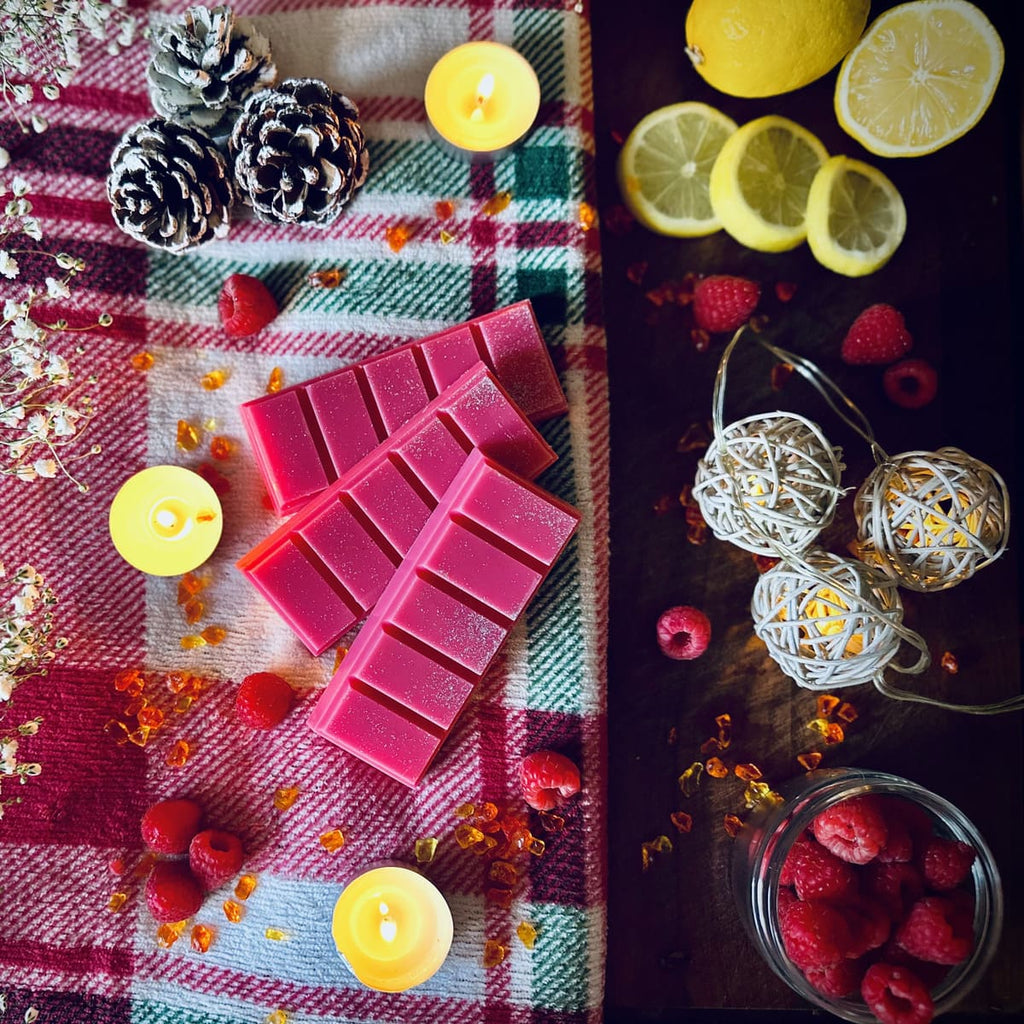 Red Christmas Wish scented snapbar wax melts on a checkered cloth with candles and berries, and lemons and berries on a dark surface.