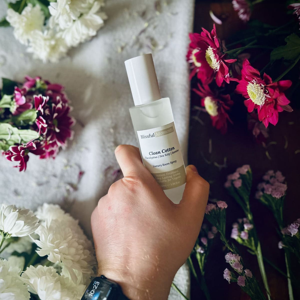 Hand holding a luxury Clean Cotton scented room spray surrounded by fresh flowers.