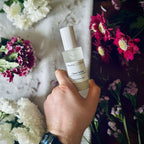 Hand holding a luxury Clean Cotton scented room spray surrounded by fresh flowers.