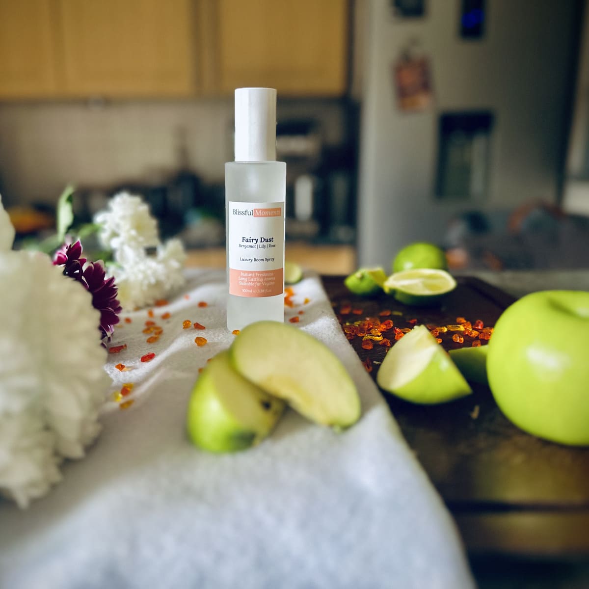 Fairy Dust scented luxury frosted glass room spray surrounded by fresh flowers, amber and green apples sitting on a cosy blanket