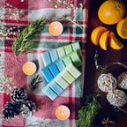 Northern lights scented snapbar wax melts on a Christmas checkered cloth with tea lights, pinecones, oranges and rosemary