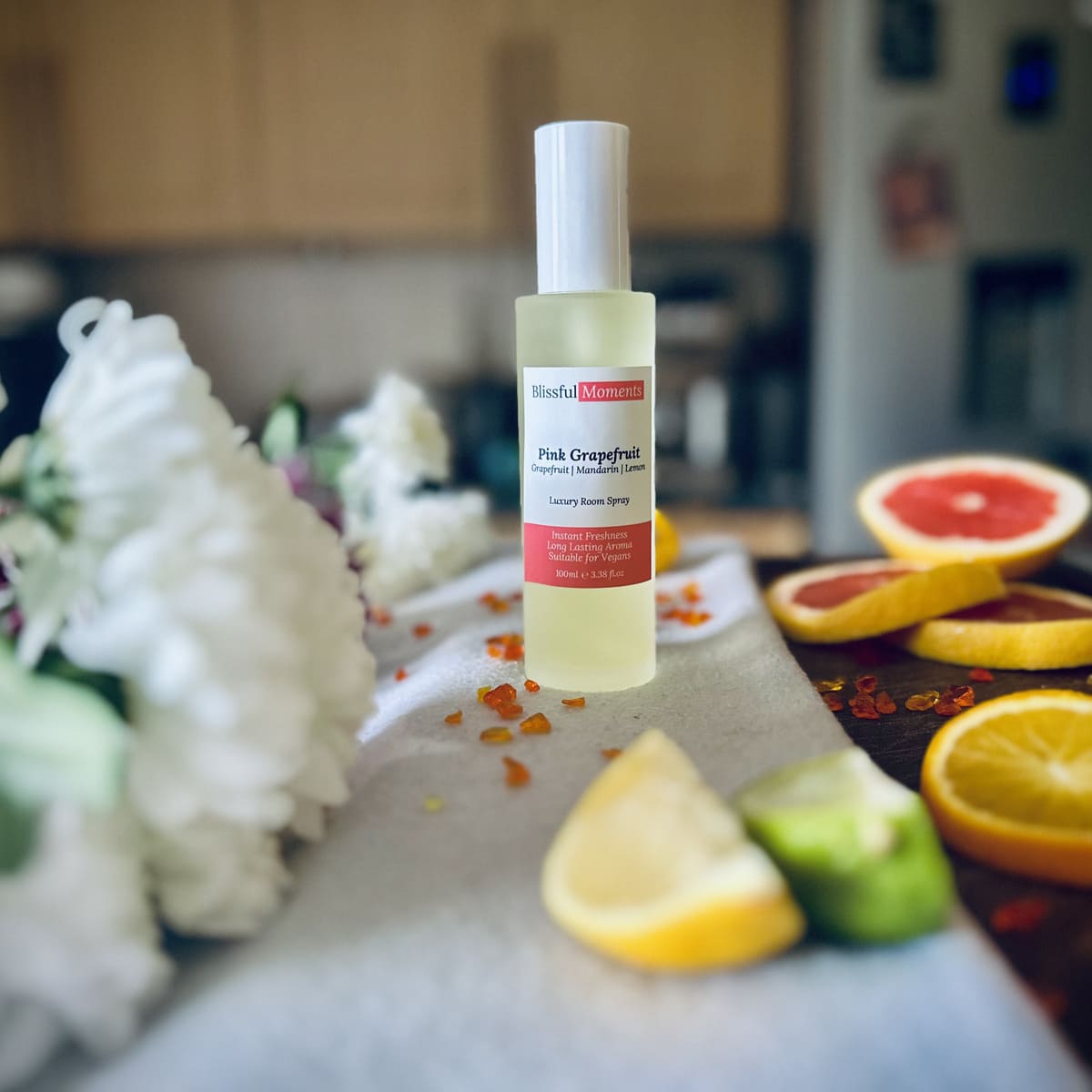 Luxury Pink Grapefruit room spray surrounded by citrus fruits and flowers sitting on a soft cosy blanket.