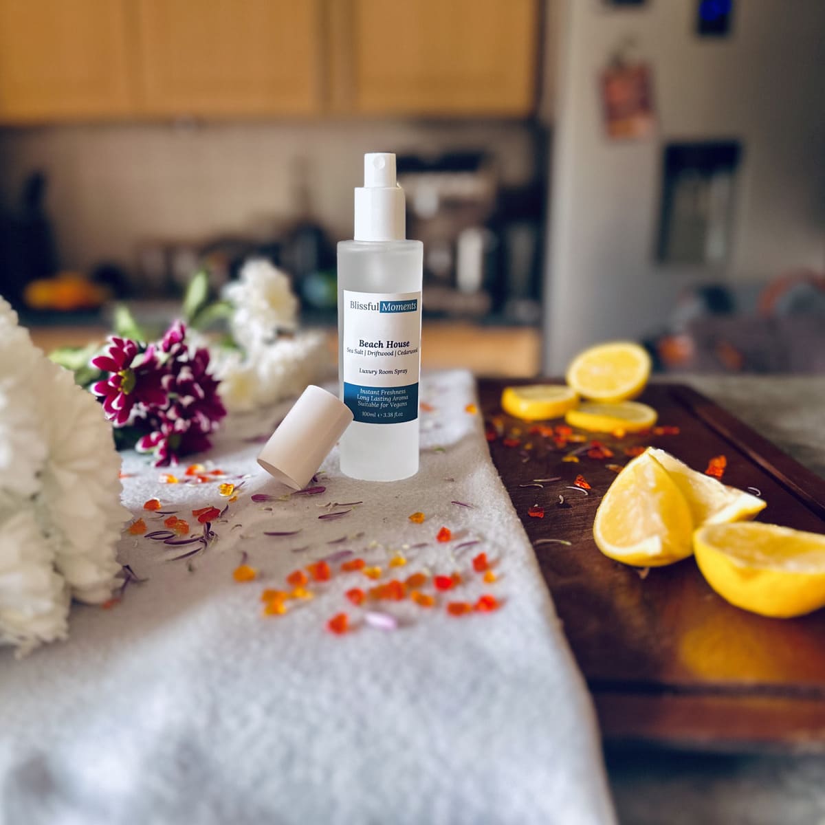  Beach House scented luxury frosted glass room spray surrounded by fresh flowers, amber and lemon sitting on a cosy blanket