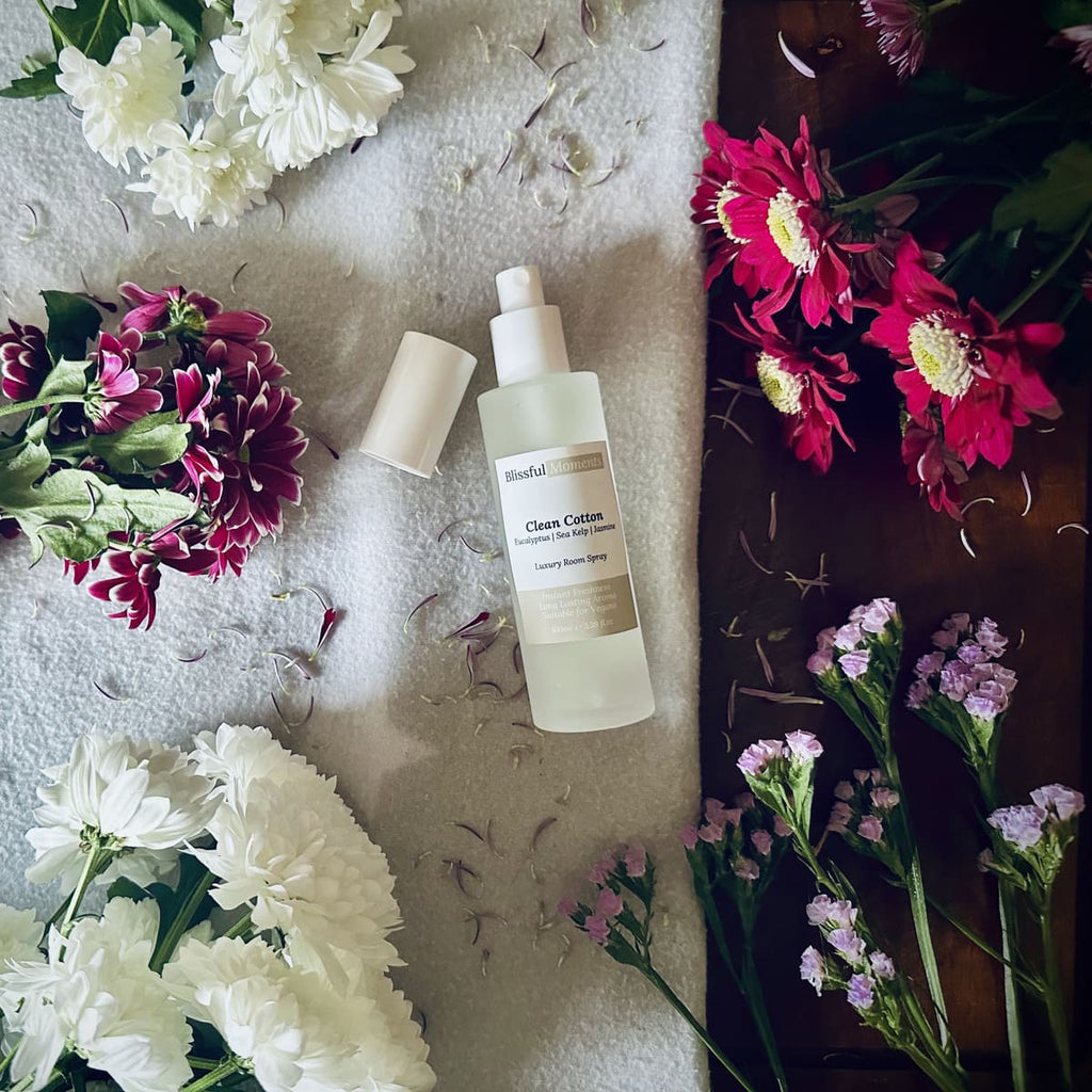 Luxury Clean Cotton scented room spray sitting on a soft cosy blanket surrounded by fresh flowers.