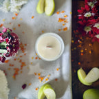Forbidden Apple scented luxury frosted glass soy candle surrounded by fresh flowers, amber and green apples sitting on a cosy blanket