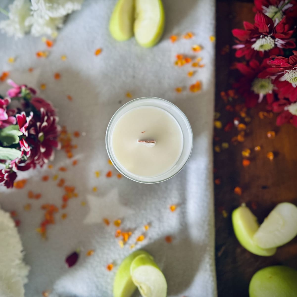Forbidden Apple scented luxury frosted glass soy candle surrounded by fresh flowers, amber and green apples sitting on a cosy blanket
