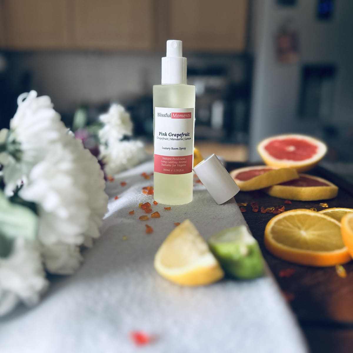 Luxury Pink Grapefruit room spray surrounded by citrus fruits and flowers sitting on a soft cosy blanket.
