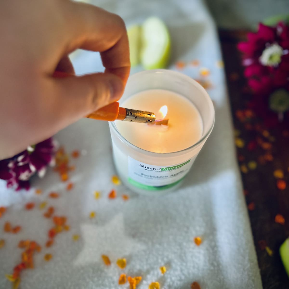 Forbidden Apple scented luxury frosted glass soy candle surrounded by fresh flowers, amber and green apples sitting on a cosy blanket