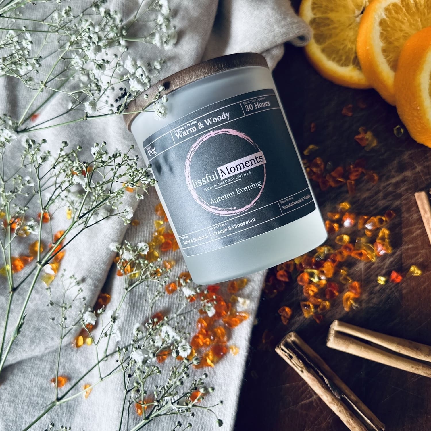 Autumn soy wax candle next to a wooly jumper and surrounde by cinnamon sticks and oranges