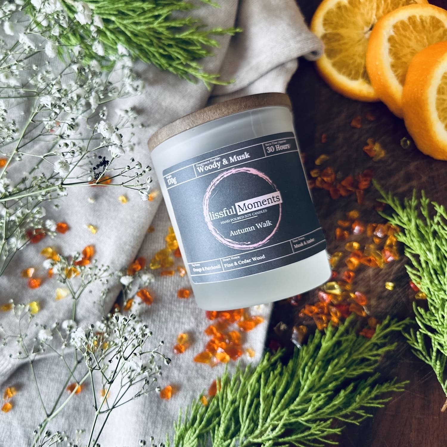 Autumn scented soy wax candle next to a wooly jumper surrounded by green leaves and orange fruits