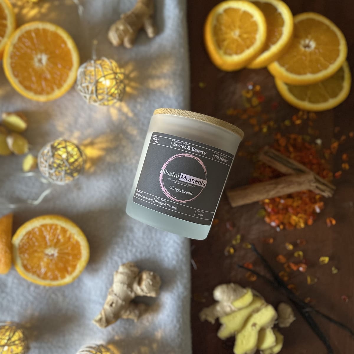 Gingerbread scented soy candle surrounded by ginger, cinnamon and oranges in a winter setting