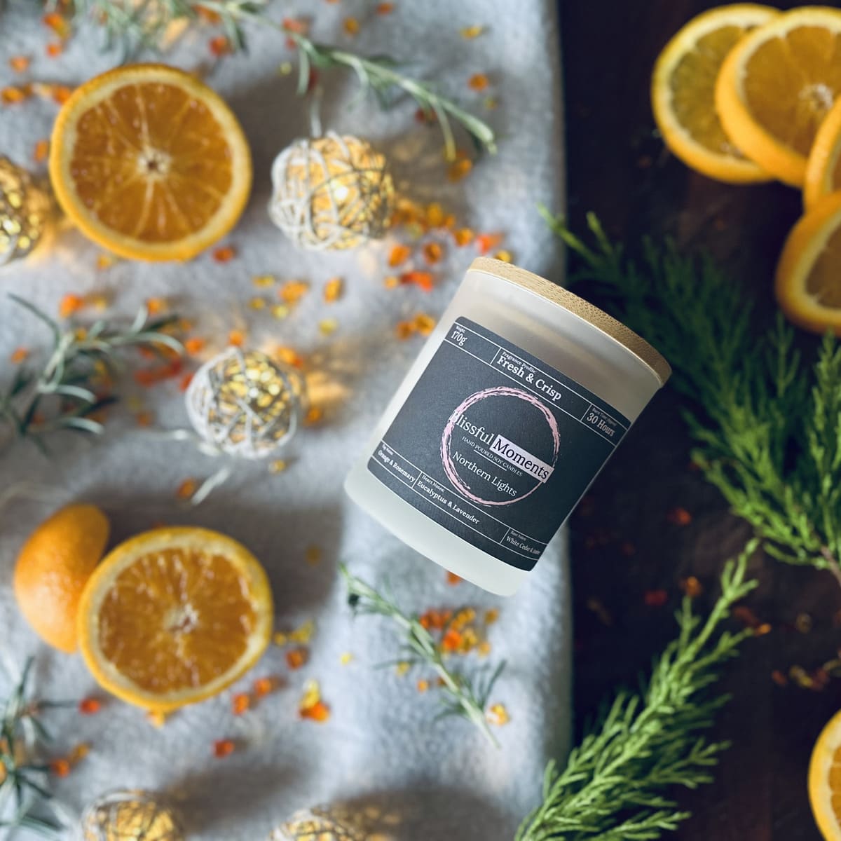 Frosted glass soy candle in a nordic setting surrounded by rosemary, citrus fruits and fairy lights