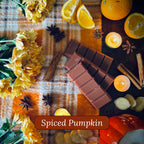 Spiced pumpkin snapbar wax melts surrounded by candles, cinnamon sticks and oranges  on a checkered fabric background.